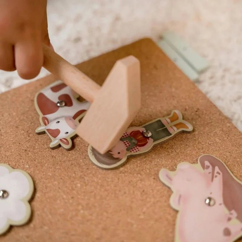 Hand using a wooden stamp on animal-themed stickers on a cork board.
