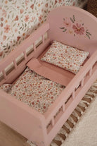 Pink crib with floral bedding and pillow against a floral wallpaper background