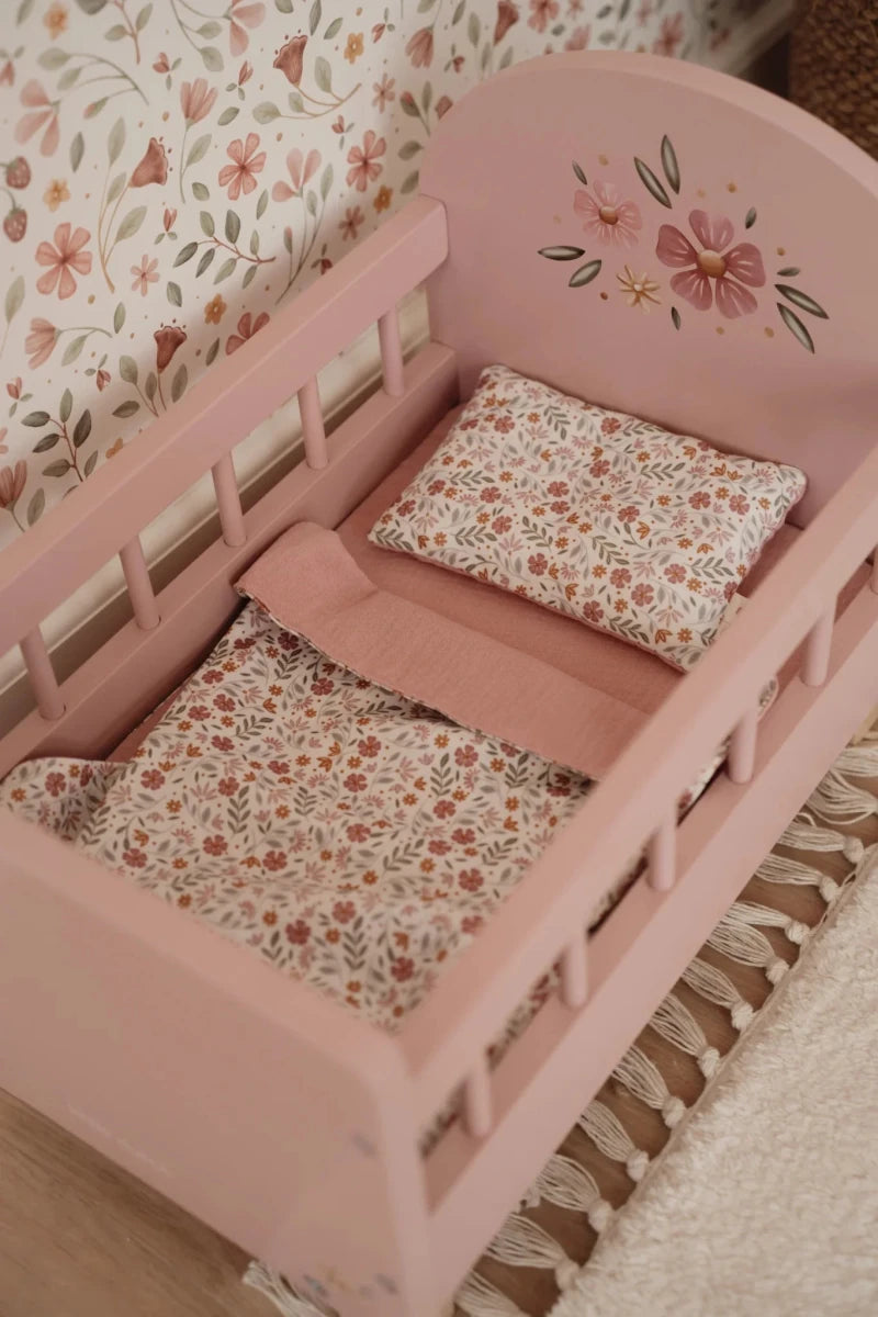 Pink crib with floral bedding and pillow against a floral wallpaper background