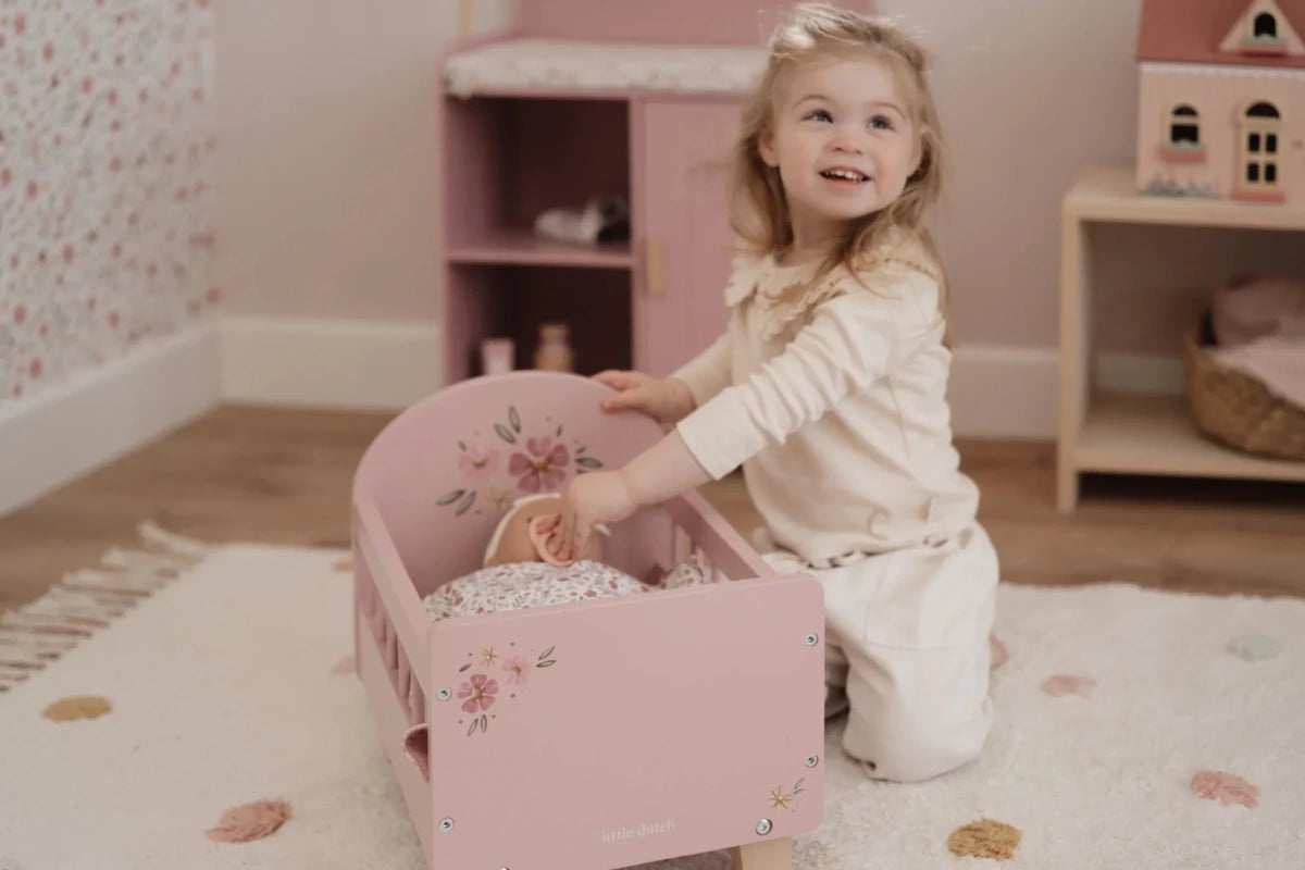 Child playing with a pink dollhouse bed in a room with floral wallpaper.