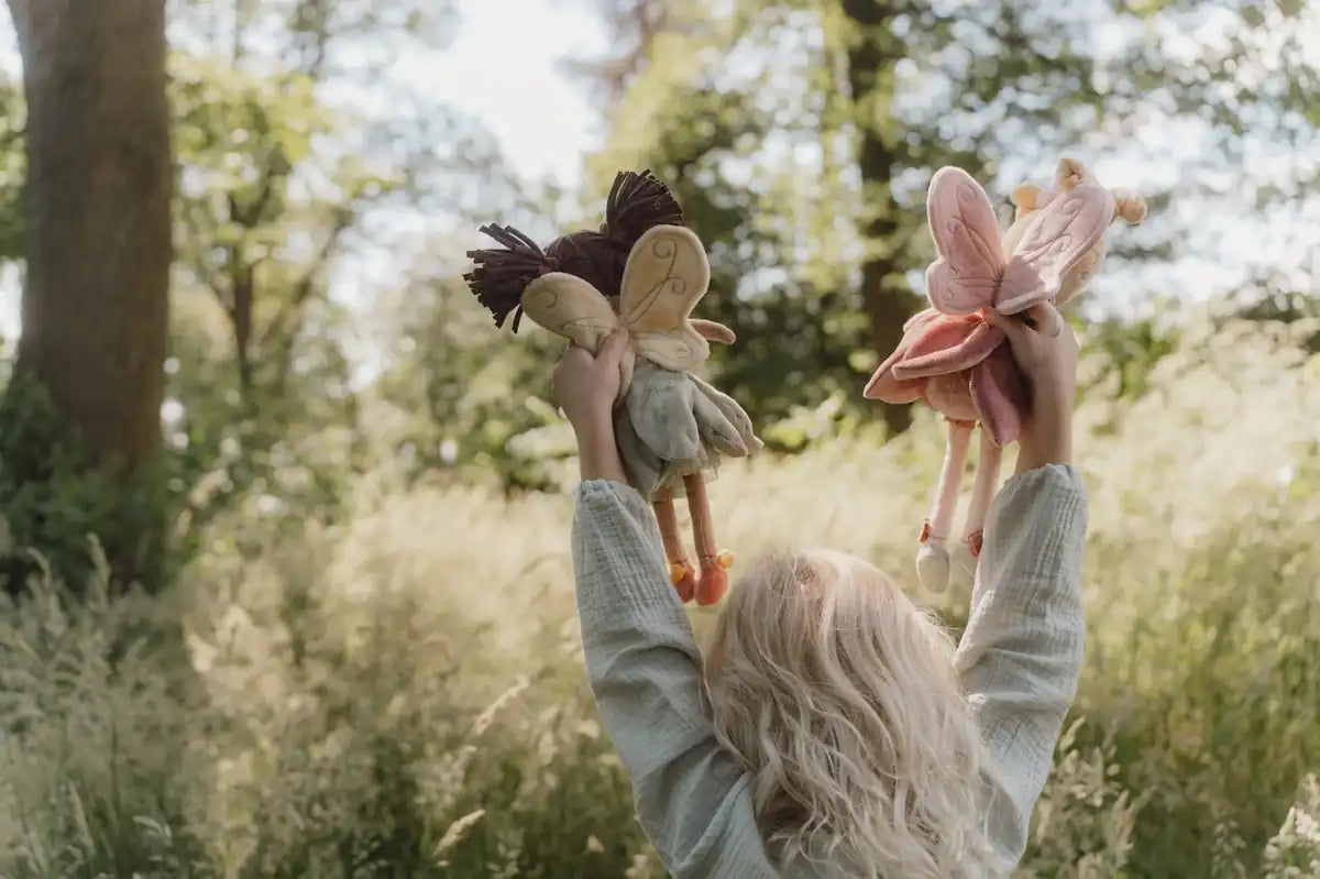 A child holding up two Little Dutch fairy dolls in a sunny meadow